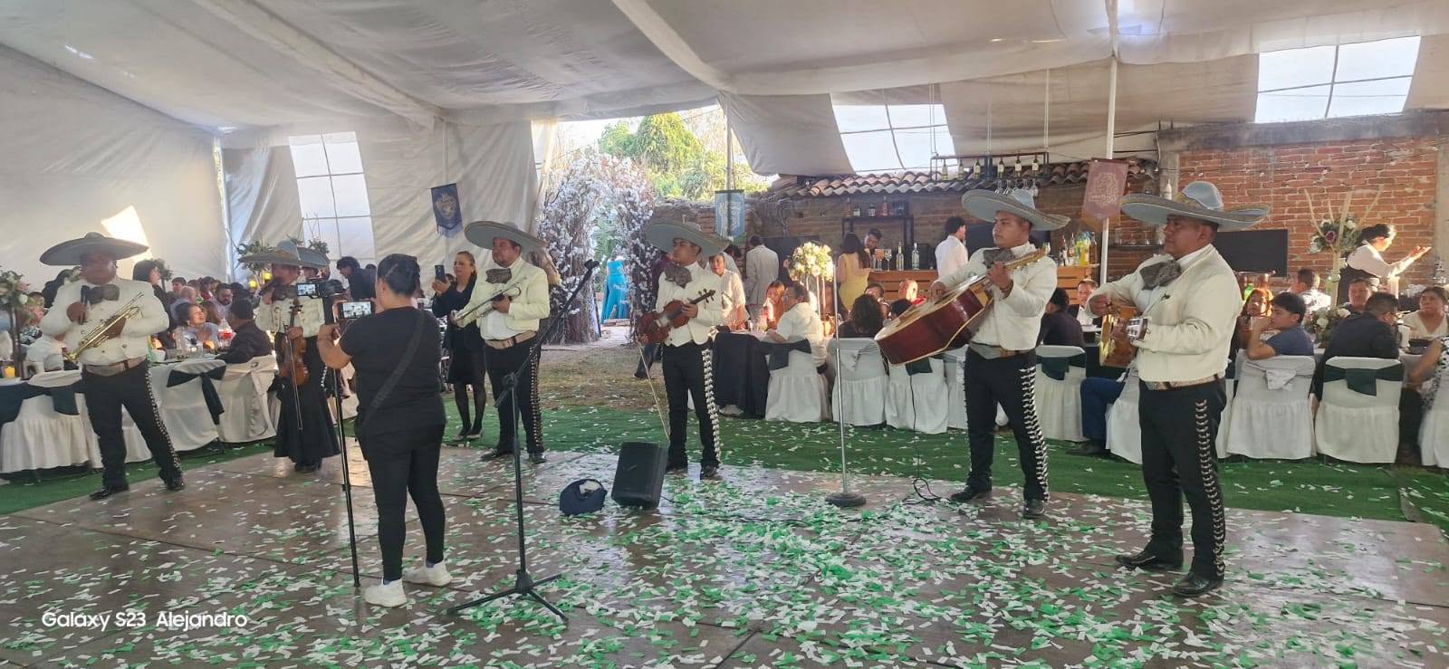Mariachi tocando en la recepción de una boda entre mesas con manteles blancos y confeti