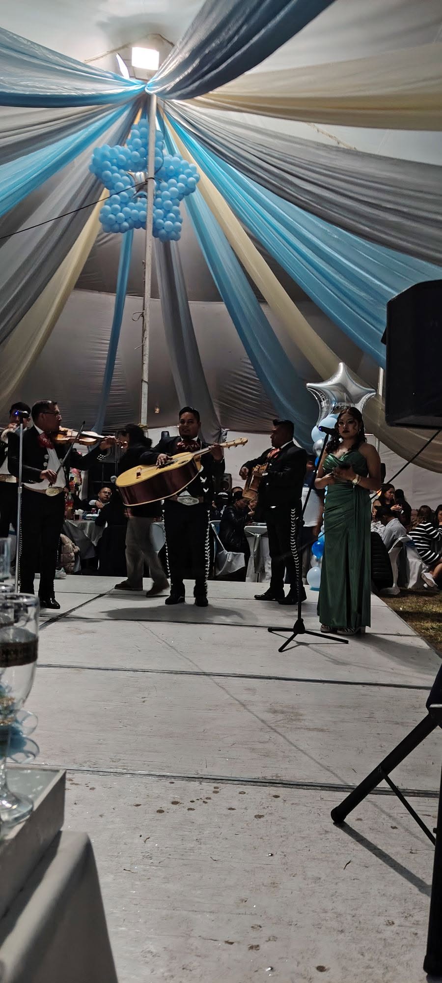 Mariachi tocando en una fiesta de XV años bajo una carpa decorada con globos azules y telas
